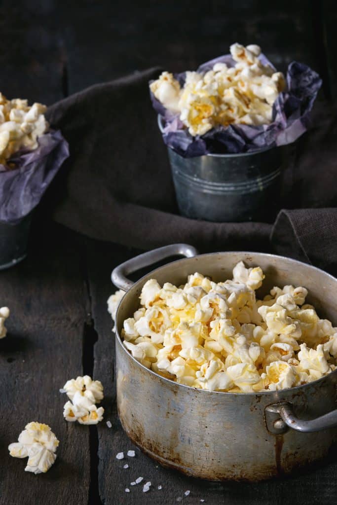 Popcorn piled into metal buckets on a dark wooden table