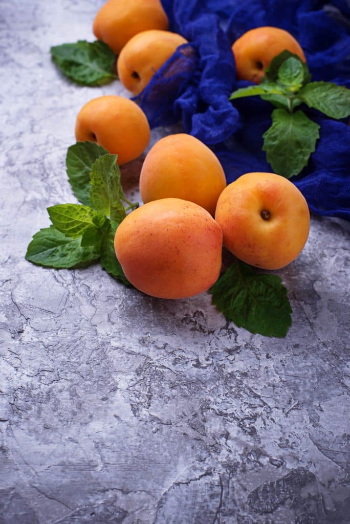 Fresh apricots arranged with mint on a gray surface
