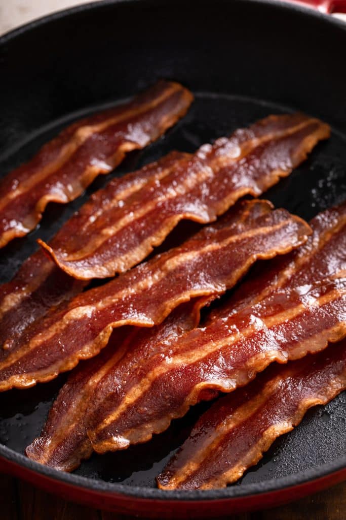 Strips of bacon cooking in a cast iron pan