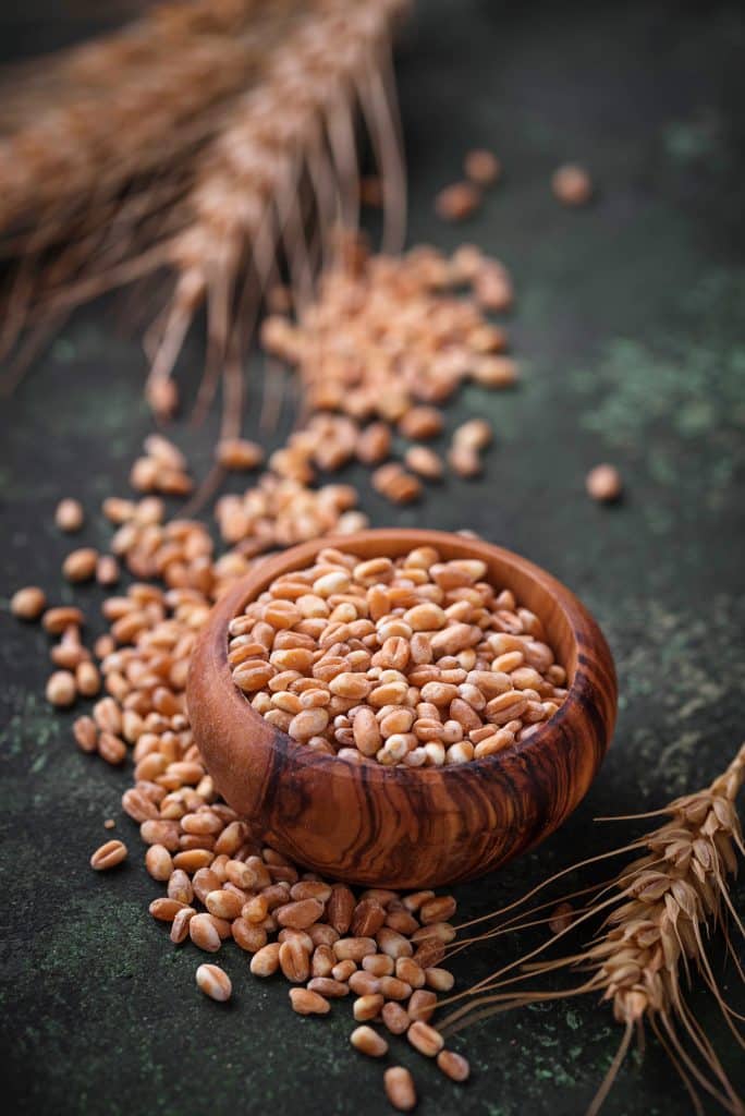 A wooden bowl filled with grain and wheat stalks