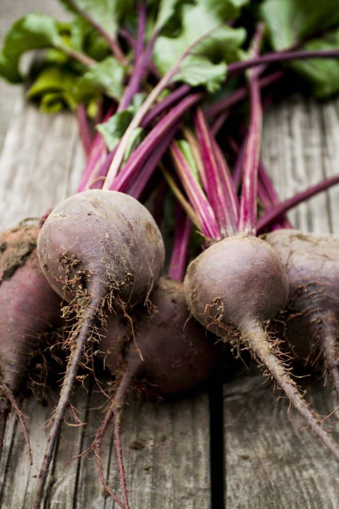Whole red beets with their leafy tops on a wooden table