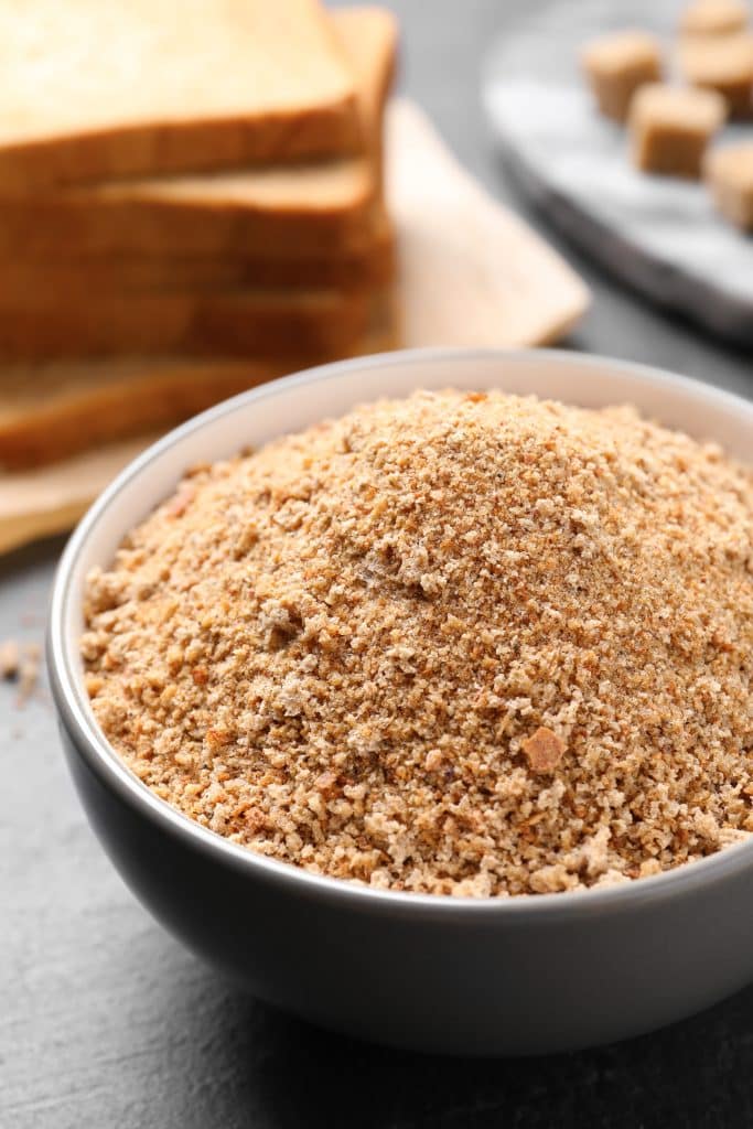 A bowl of fresh bread crumbs next to sliced bread