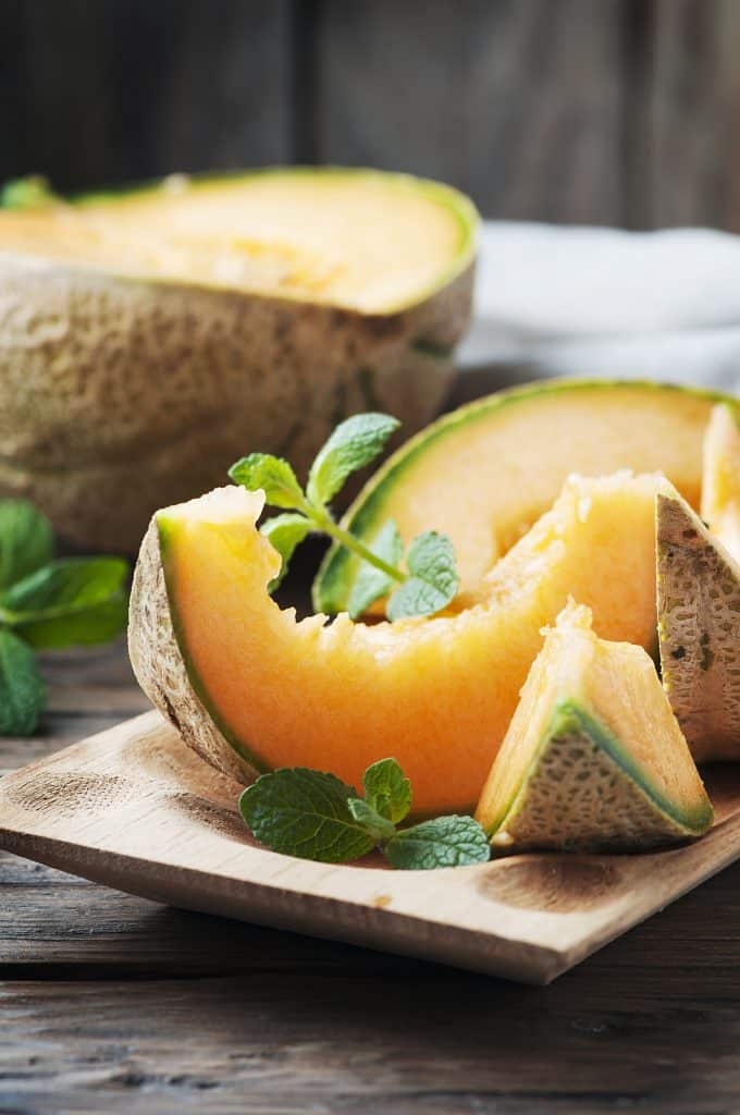 Cantaloupe slices with mint on a wooden board