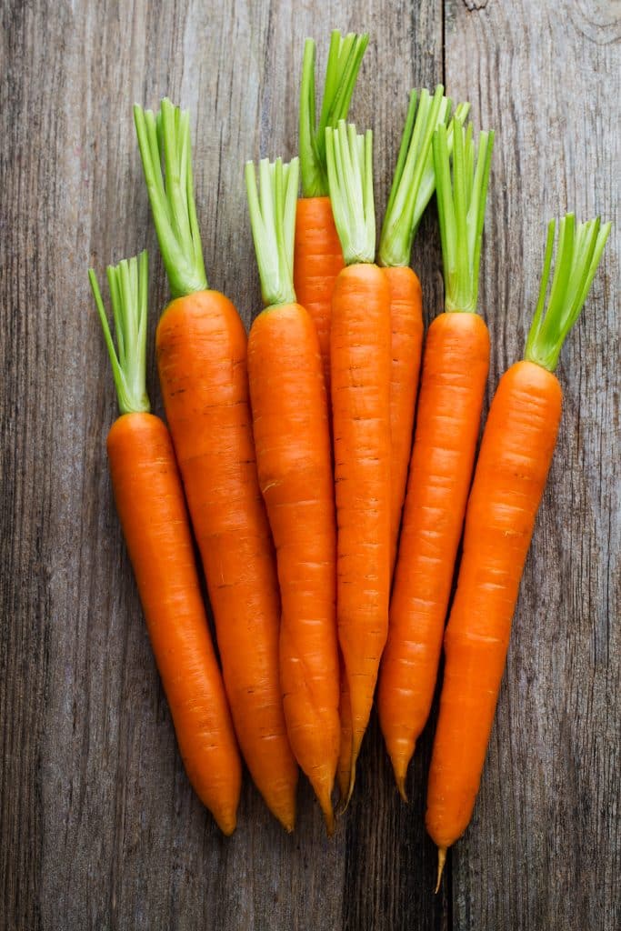 Whole carrots with green stems laid on a wooden cutting surface