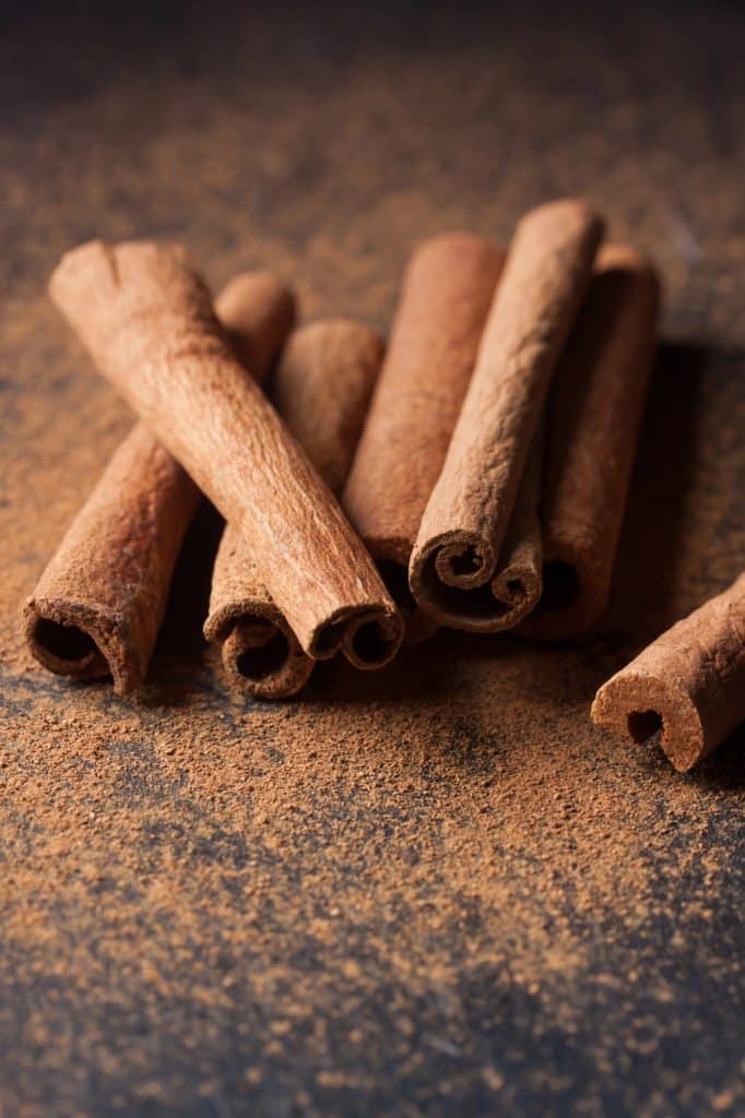 Ground cinnamon and cinnamon sticks on a wooden surface