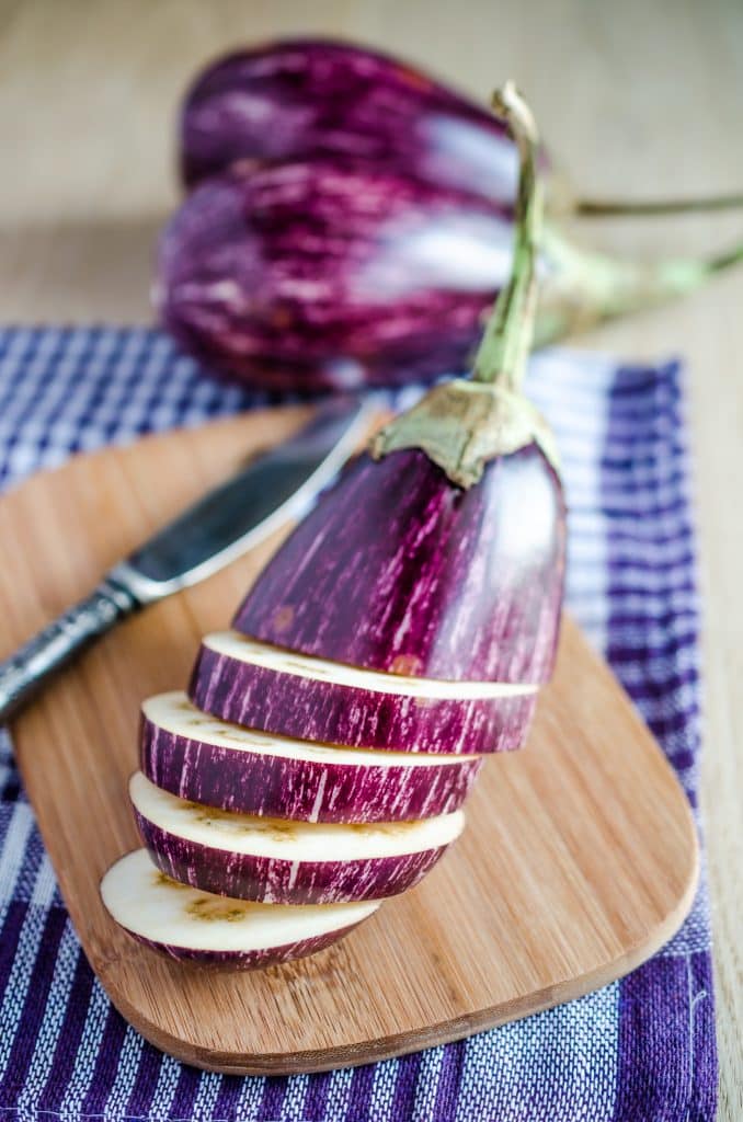 Sliced eggplant on a cutting board beside a knife