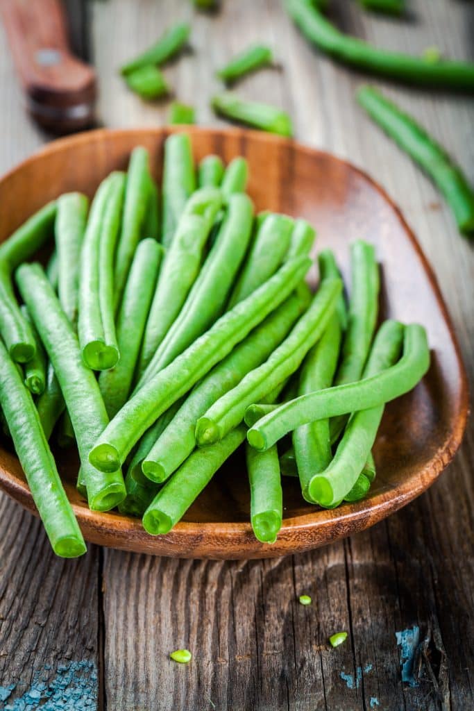 Fresh green bean pods piled in a wooden bowl
