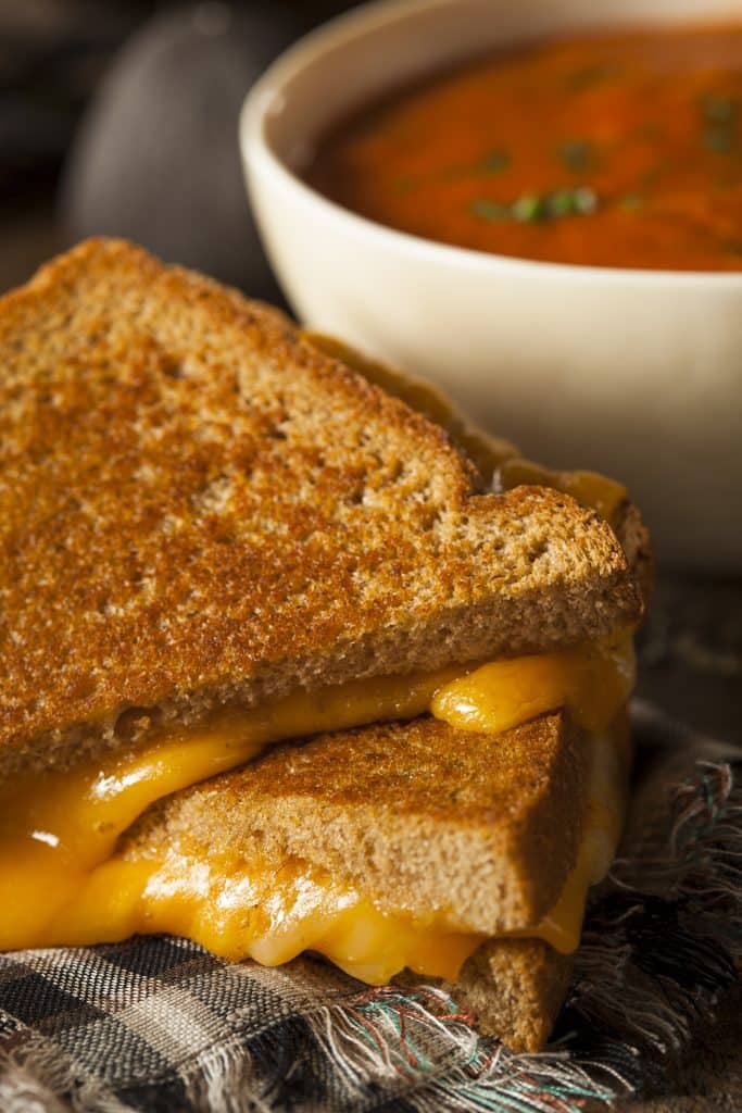 Golden grilled cheese sandwich next to a bowl of tomato soup