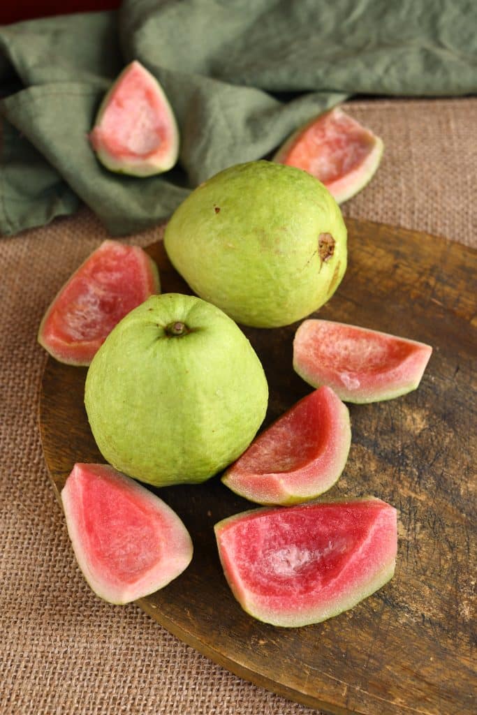 Fresh green guavas next to pink guava slices
