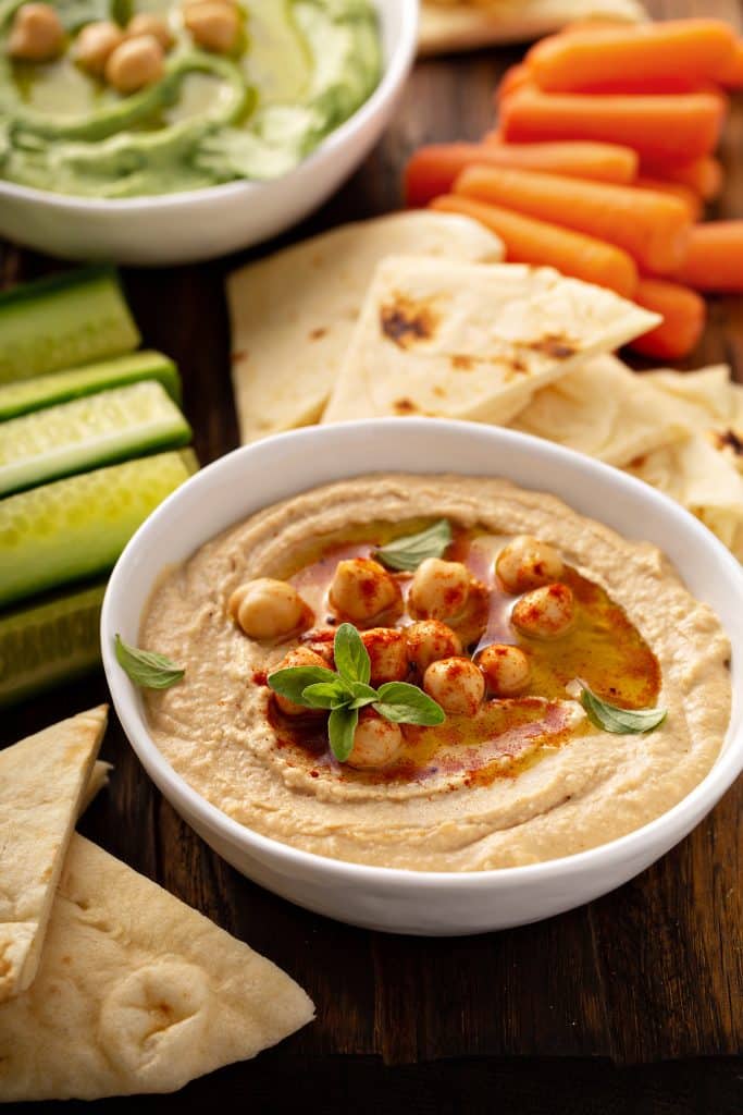 A bowl of hummus surrounded by vegetables and pita