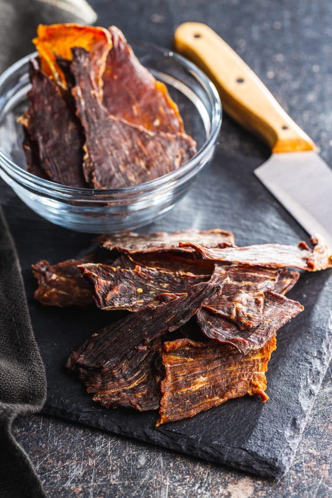 Sliced beef jerky next to a cutting knife