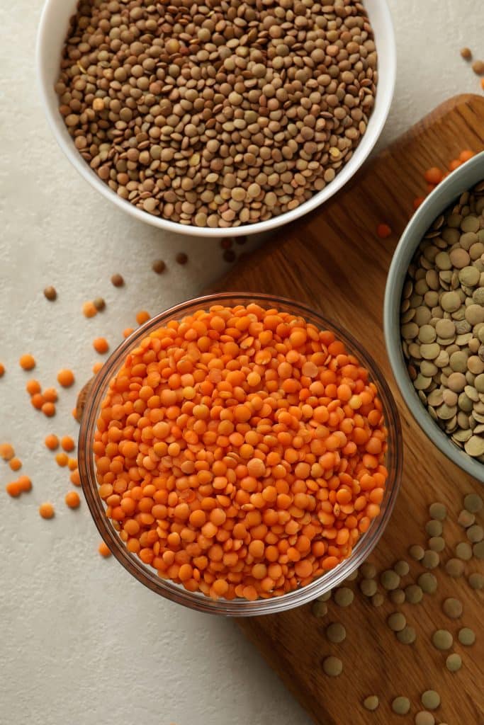 Three bowls of colorful dried lentils on a wood board