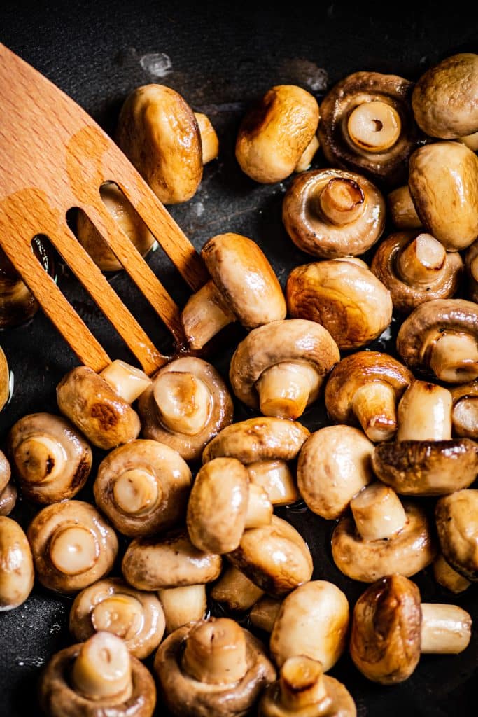 Sauteed mushrooms being stirred with a wooden spatula