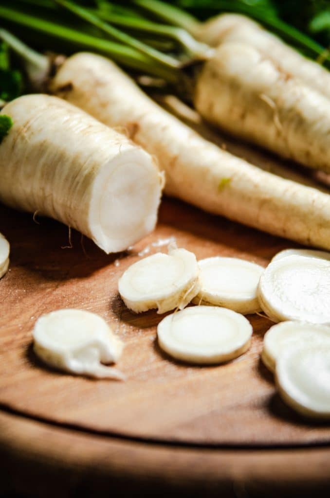 Fresh parsnip roots and slices on a wooden surface
