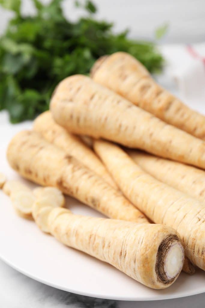 Fresh parsnips with green tops arranged on a white plate