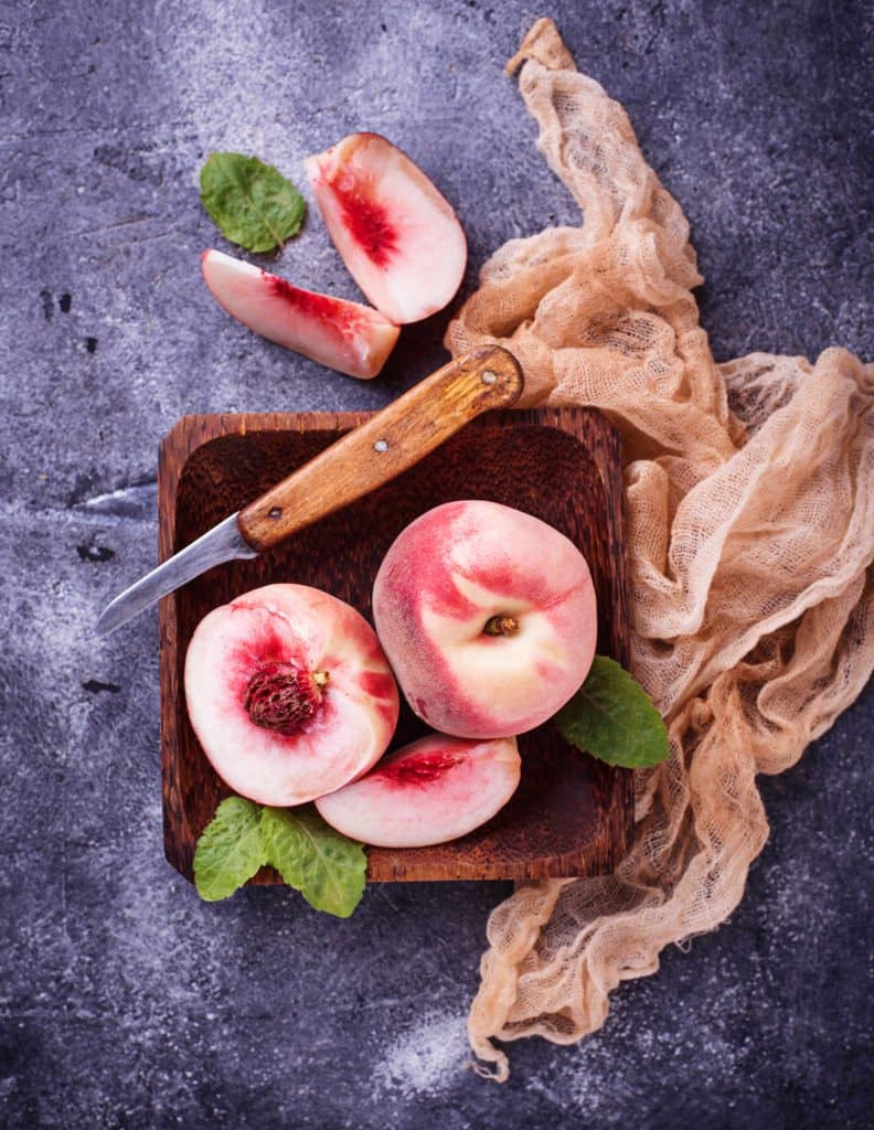 Sliced fresh peaches with a knife on a wooden board