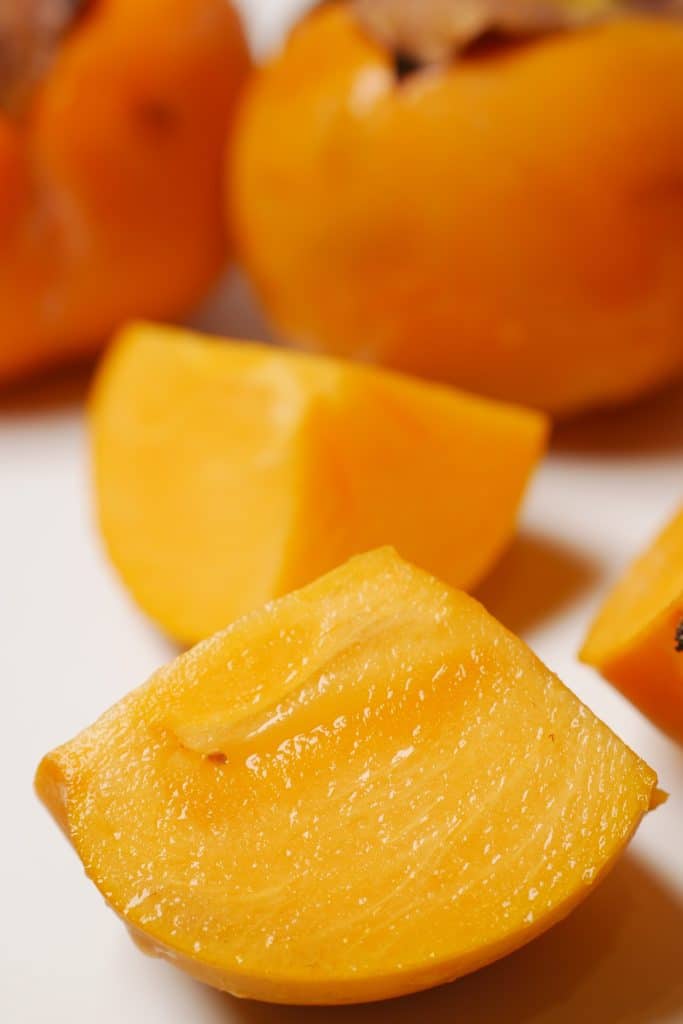 Bright orange persimmon slices on a white surface