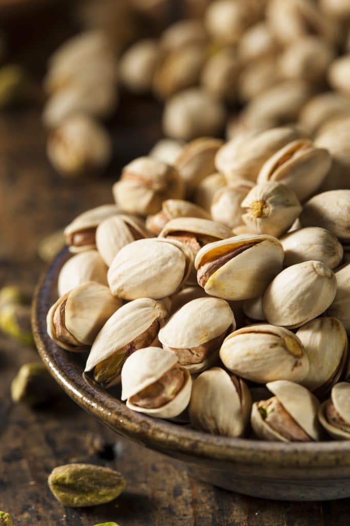 A wooden bowl of pistachios in their shells