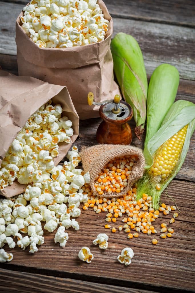 Popped popcorn and loose corn kernels on a wooden table