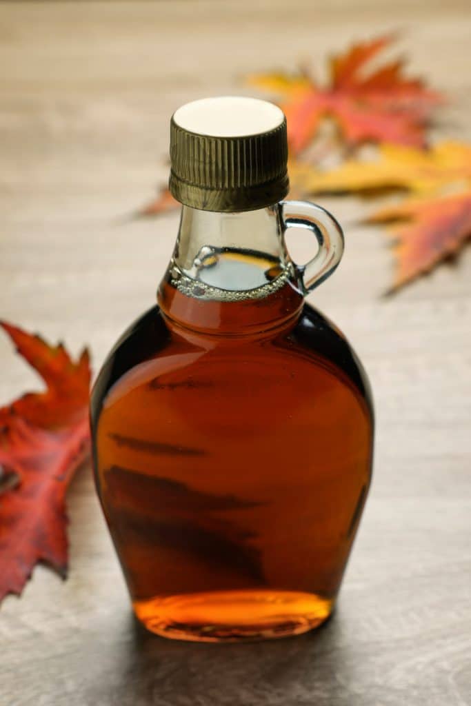 A jar of maple syrup surrounded by fall leaves