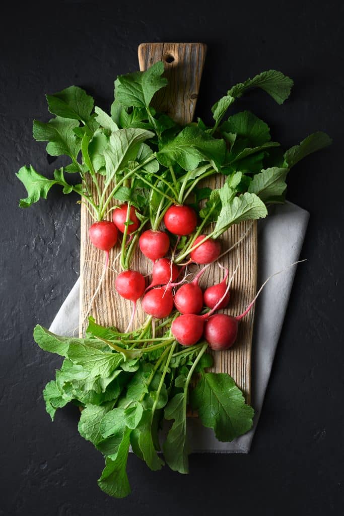 Fresh red radishes on a rustic wooden cutting board