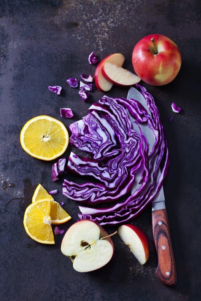 Fresh red cabbage next to apples and oranges