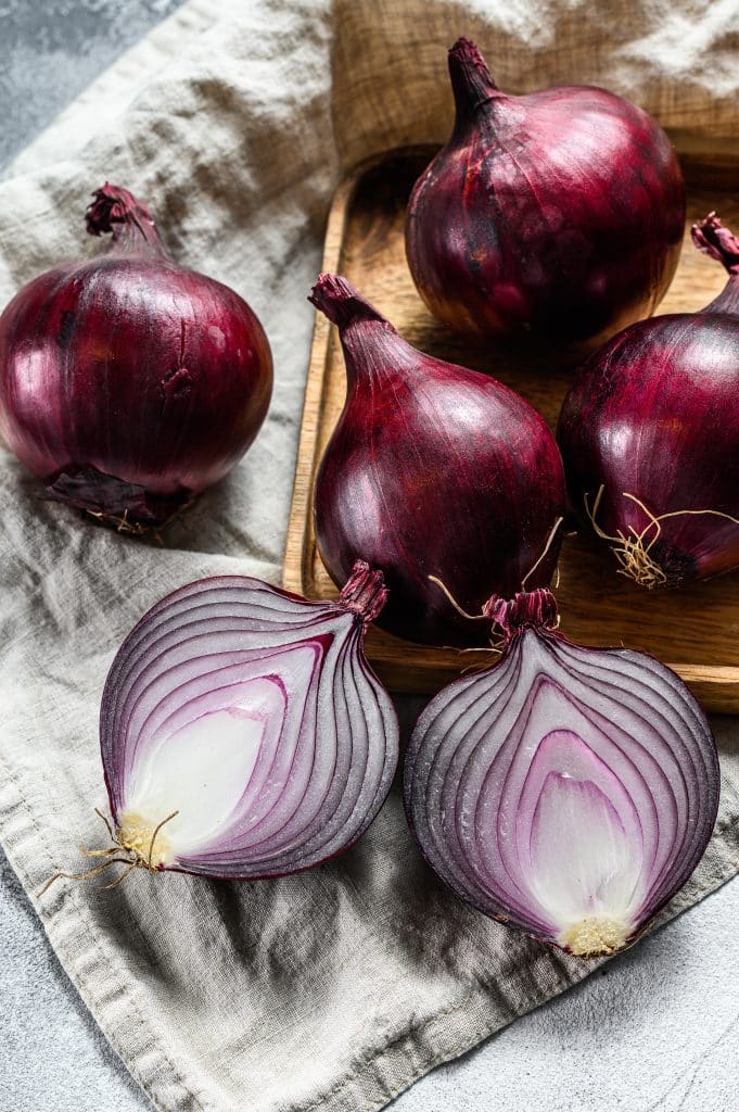 Halved red onions sitting in a wooden bowl