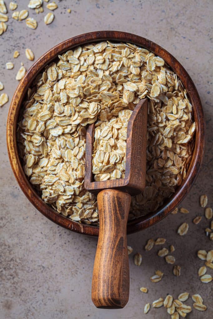 A wooden bowl of rolled oats with a scoop