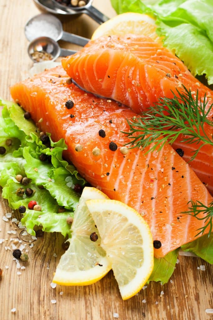 Raw salmon fillets with lemon slices and fresh greens