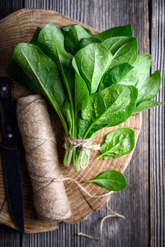 Fresh spinach leaves laid out on a wooden board