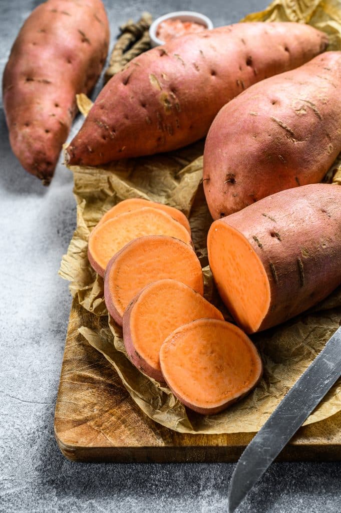 A raw sweet potato on a wooden chopping board
