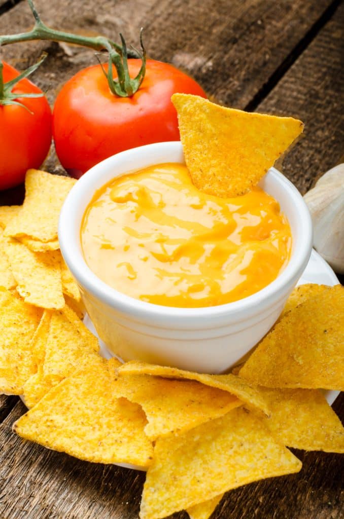 A pot of melted cheese dip with tomatoes and chips